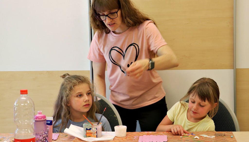 Jugendhaus-Leiterin Ulrike Paul (M.) gibt den sechsjährigen Mädchen Hetty (li.) und Lea (re.) Tipps, wie ihr Beach-Schild weiter gestaltet werden kann.