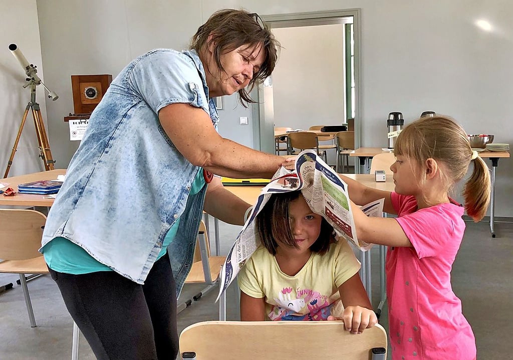 Cornelia Lorenz, Leiterin der Umweltschule Wethau, gestaltet mit Amalia und Sophia eine Hut aus Zeitungspapier.