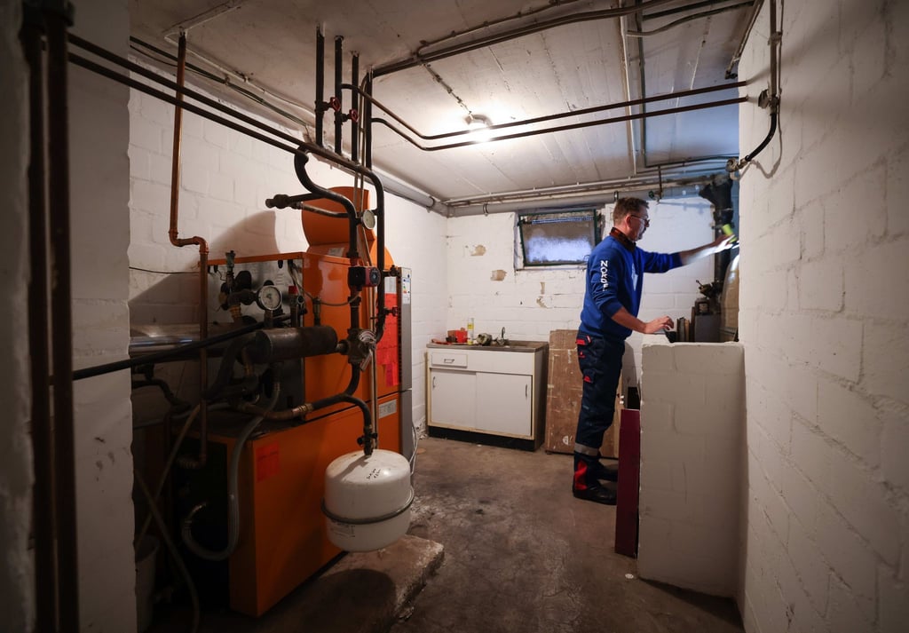 Ein Mitarbeiter eines Diesel- und Heizöl-Unternehmens prüft die beiden Kunststofftanks in einem Heizungskeller bei der Heizöllieferung in einem Einfamilienhaus.