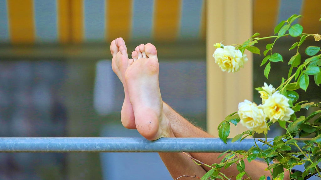 Ein Mann liegt auf seinem Balkon und hat seine Beine auf das Balkongeländer gelegt. Ob er sich dort unbekleidet sonnt, verrät dieses Foto nicht.  Grundsätzlich dürfte er das – solange es die Nachbarn nicht stört.
