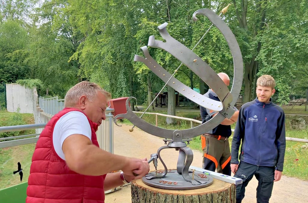 Nils Tölle schraubt die Sonnenuhr fest. Tierparkleiter Nils Becker (rechts) freut sich über den neuen Hingucker.