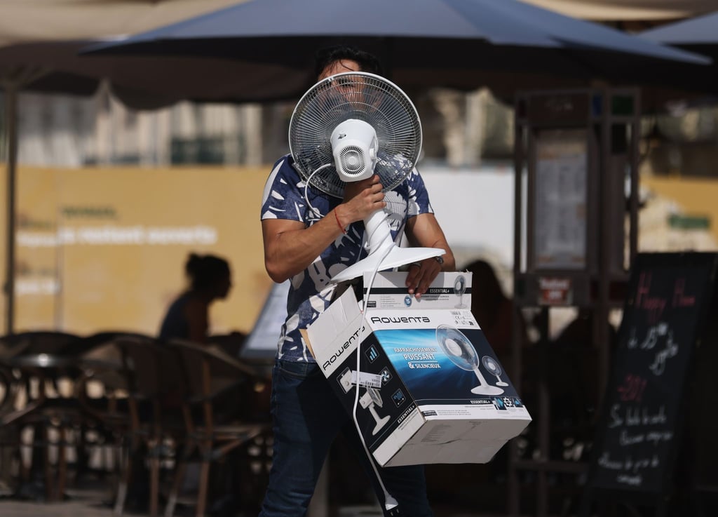 Ein Mann trägt einen Ventilator, während er bei 38 Grad Celsius über die Place de la Comedie in Montpellier geht.