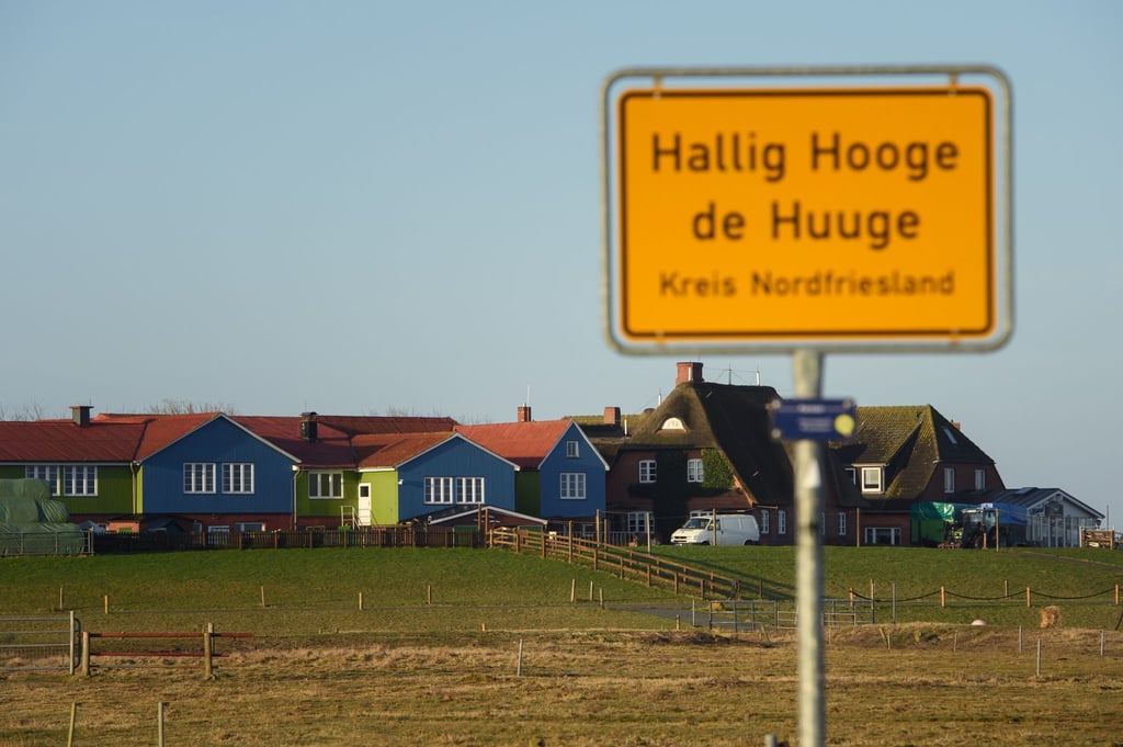 Bunte Häuser sind auf einer Warft auf Hallig Hooge hinter dem Ortsschild zu sehen.