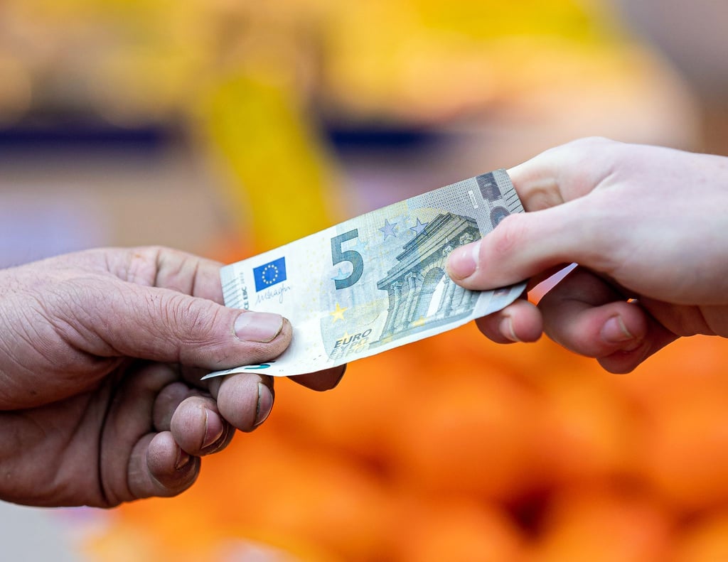 Ein Kunde bezahlt seinen Einkauf an einem Stand auf einem Wochenmarkt mit einem Fünf-Euro-Schein.
