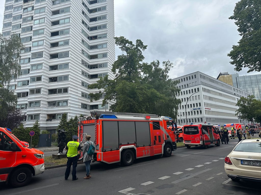 Einsatzkräfte stehen vor dem Hochhaus auf der Straße.
