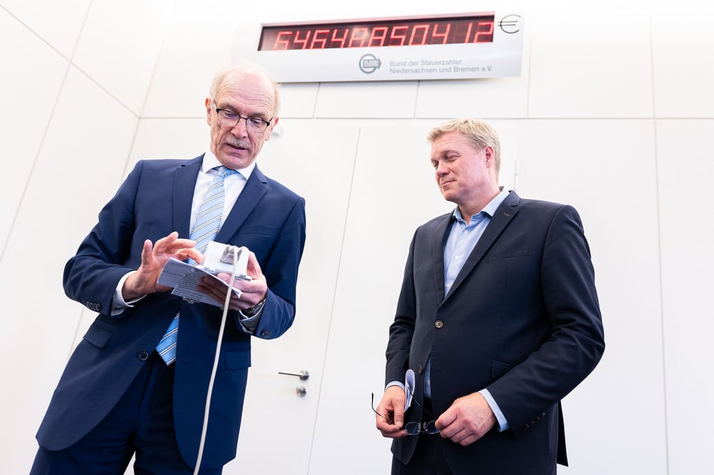 Bernhard Zentgraf (l) stellt die Schuldenuhr für Niedersachsen im Niedersächsischen Landtag neu ein.