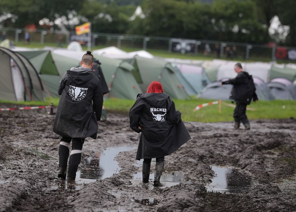 Metal-Fans sind auf dem schlammigen Festivalgelände unterwegs.