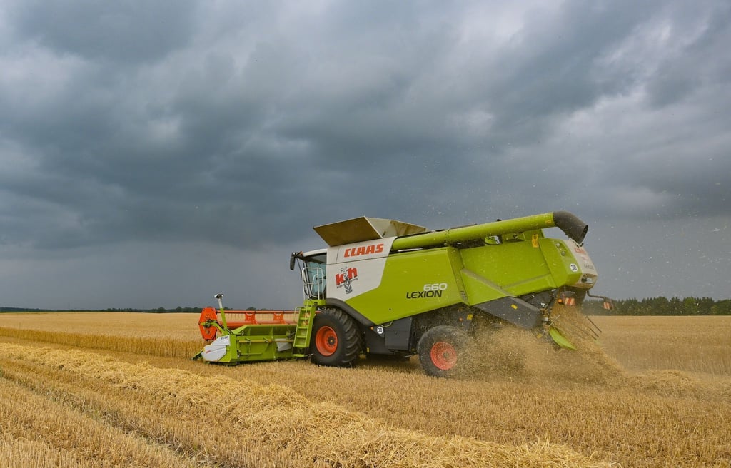 Gewitterwolken ziehen über ein Feld, wo gerade ein Landwirt mit seinem Wintergerste erntet.