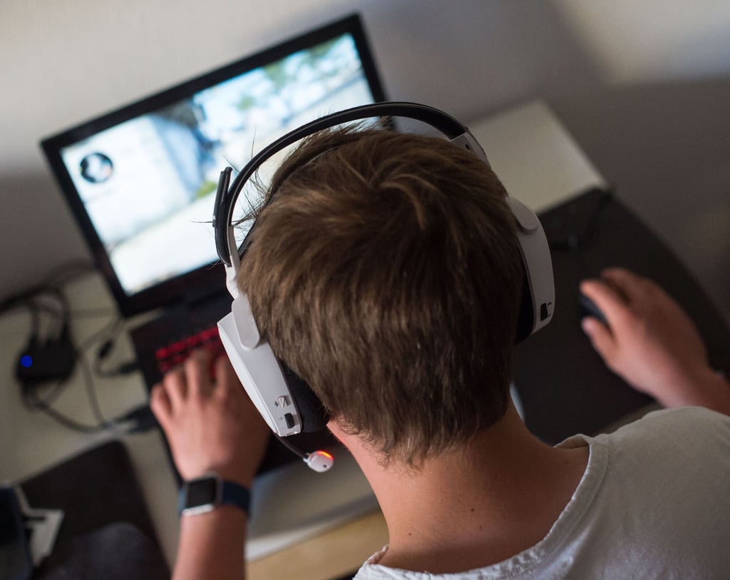 Ein Jugendlicher sitzt mit einem Headset vor einem Laptop und spielt ein Computerspiel.