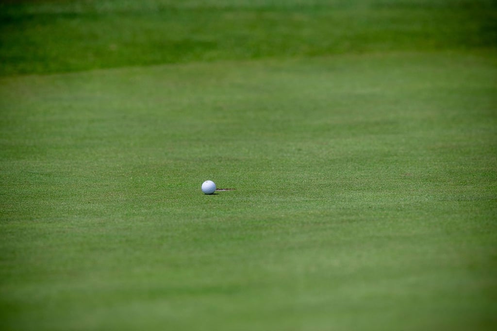 Ein Golfball liegt wenige Zentimeter vor dem Loch.