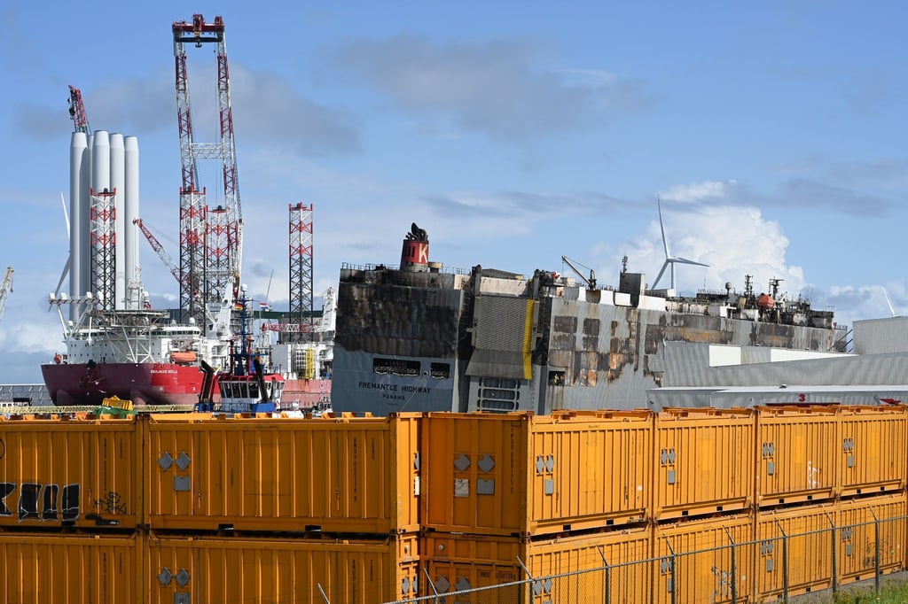 Der schwer beschädigte Autofrachter „Fremantle Highway„ wird durch gelbe Container abgeschirmt.