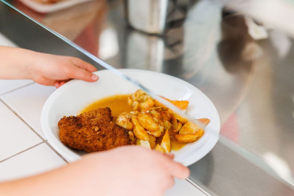 Ein Mädchen nimmt einen Teller mit Schnitzel, Kartoffeln und Sauce vom Tresen.