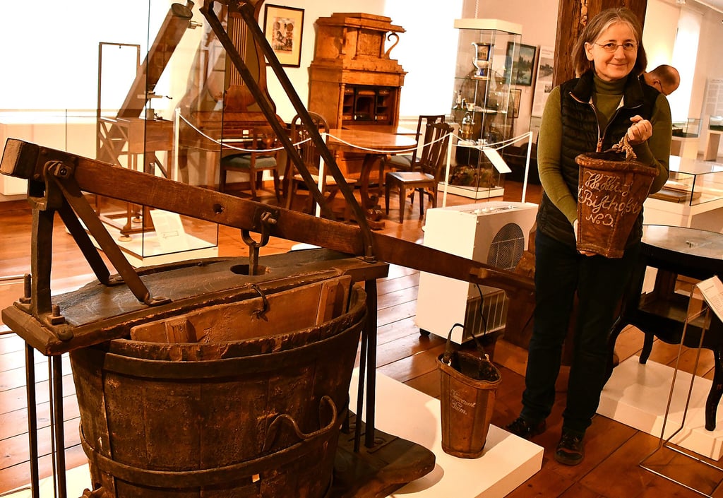 Museumsleiterin Antje Reichel zeigt einen ledernen Eimer, den jeder Hausbesitzer vorzuhalten hatte. Brannte es, wurde die Feuerwehrspritze über Eimerketten mit Wasser gefüllt.