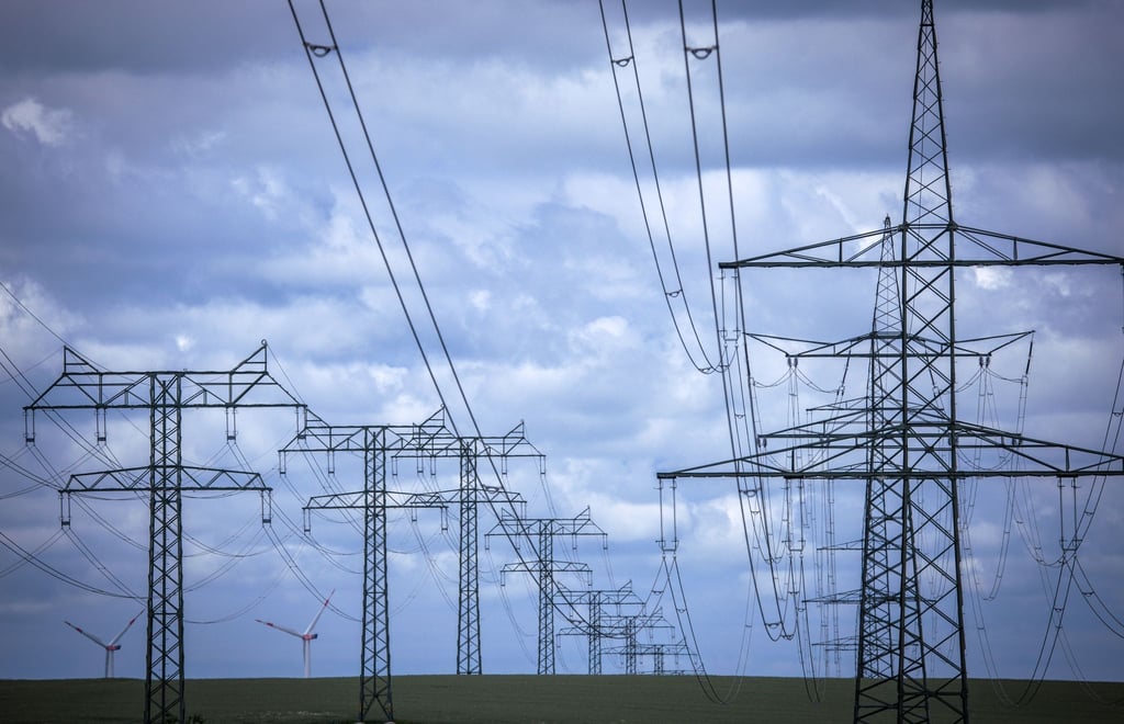 Mehrere Leitungen für die Übertragung von Strom. Im Hintergrund sind Windräder erkennbar.