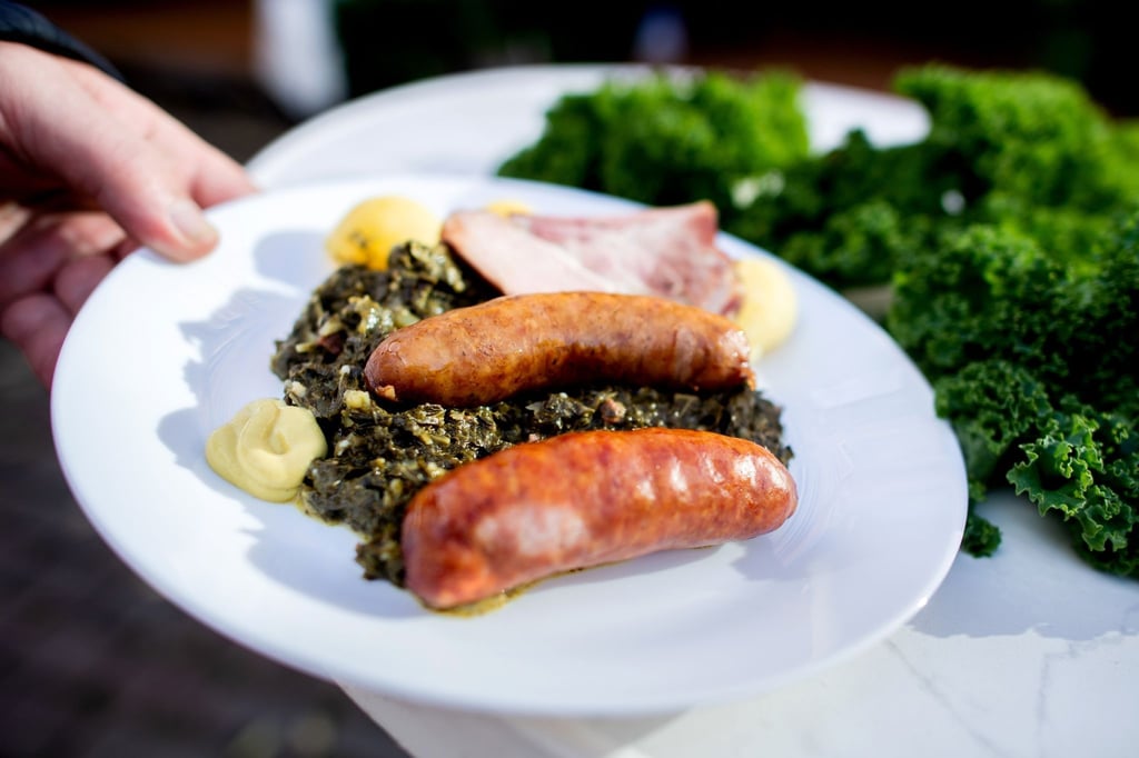Ein Besucher hält auf dem Rathausmarkt einen Teller mit einer Portion Grünkohl und den Beilagen Salzkartoffeln, Kochwurst, Pinkelwurst und Kasseler in den Händen.