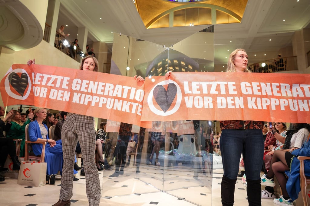 Demonstrantinnen der Gruppe „Letzte Generation“ halten Transparente bei der Fashion Show der Designerin Anja Gockel.