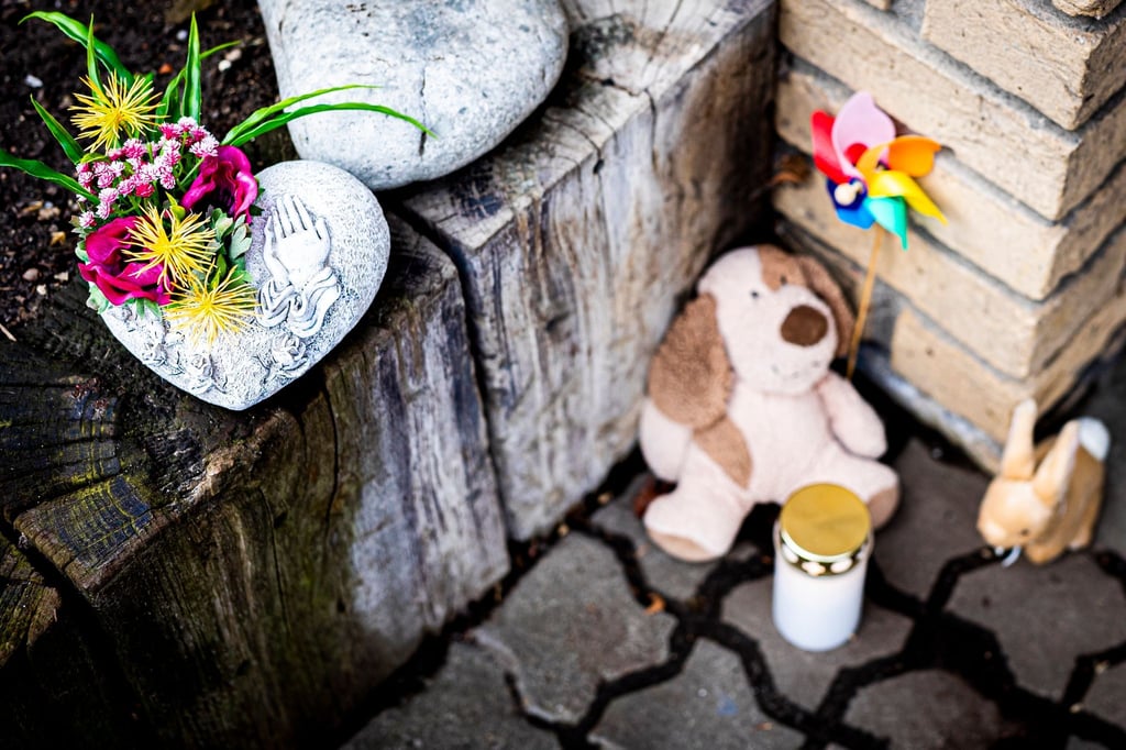 Blumen, zwei Plüschtiere und ein Windspiel liegen neben einer Grabkerze an einem Hauseingang.