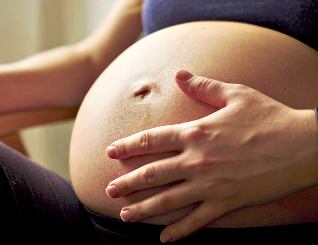 Eine schwangere Frau hält sich ihren Babybauch.