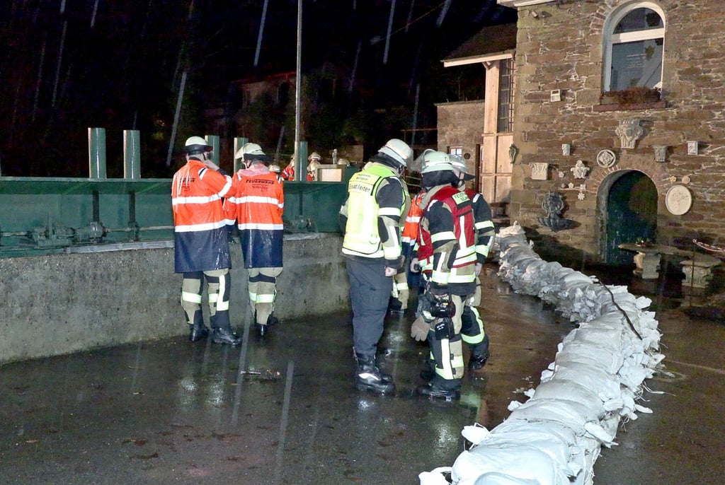 Einsatzkräfte der Feuerwehr auf einer durch Dauerregen überfluteten Straße in Solingen.