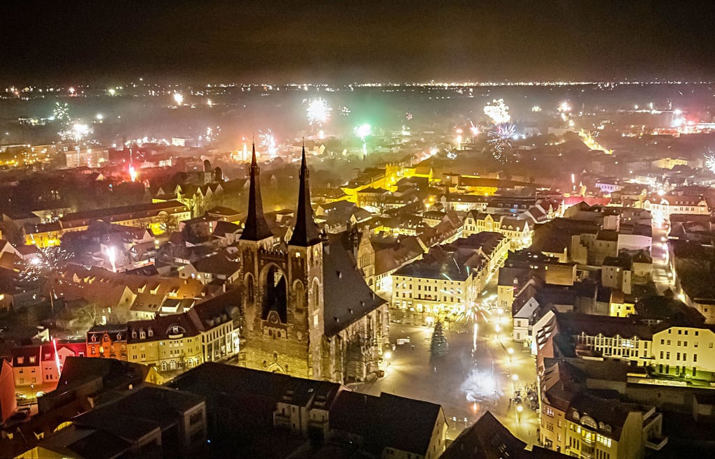 Mit Feuerwerk feiern die Menschen den Jahreswechsel. Die Kirche St. Jakob mit den mit 75 Metern höchsten Türmen in Anhalt wird angestrahlt.