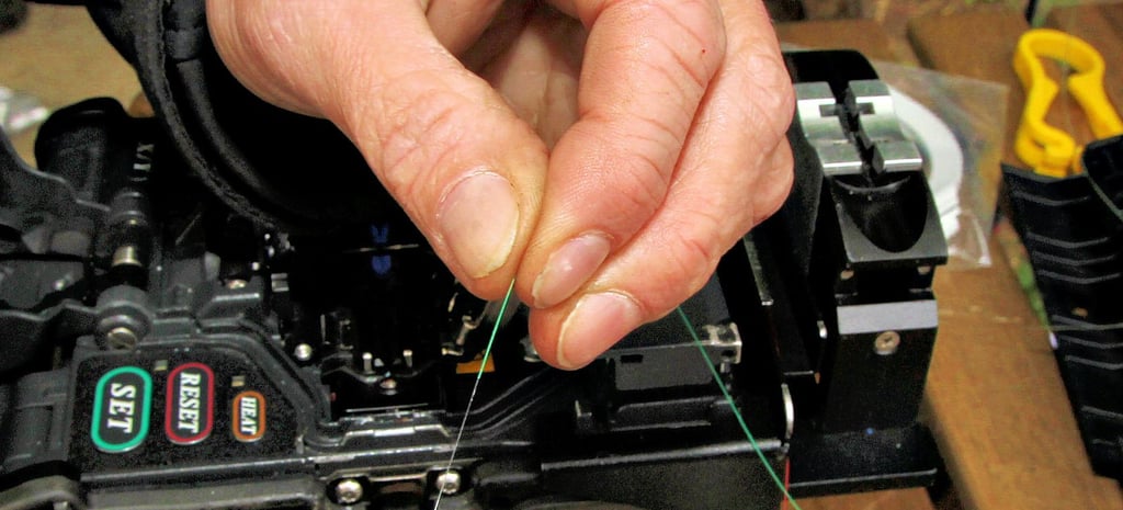 Ein Glasfaserkabel in der Hand eines Technikers, der die Kabel miteinander verbindet. Die Faser ist dabei dünner als ein menschliches Haar.