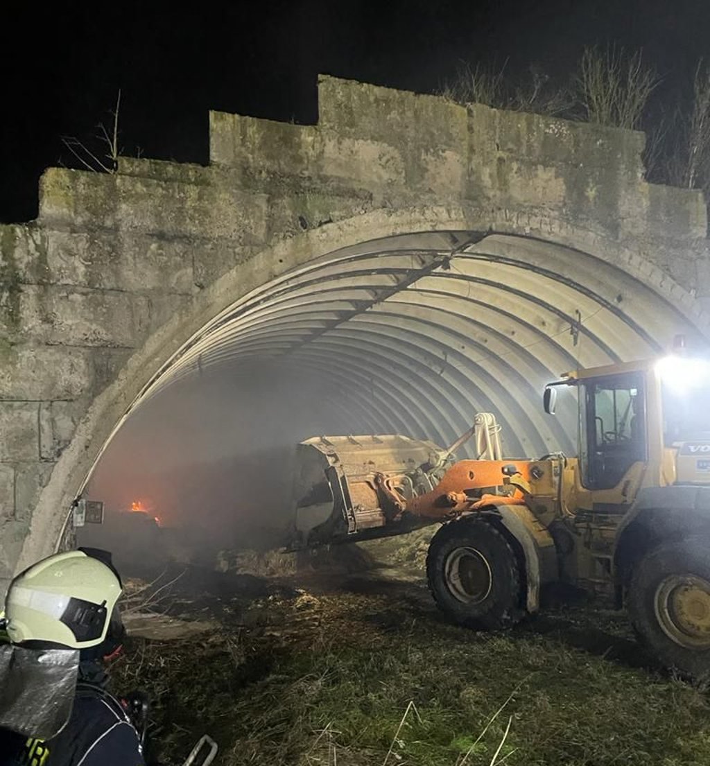 Feuerwehr und WImex-Leute löschen brennende Strohballen in einem Hangar.