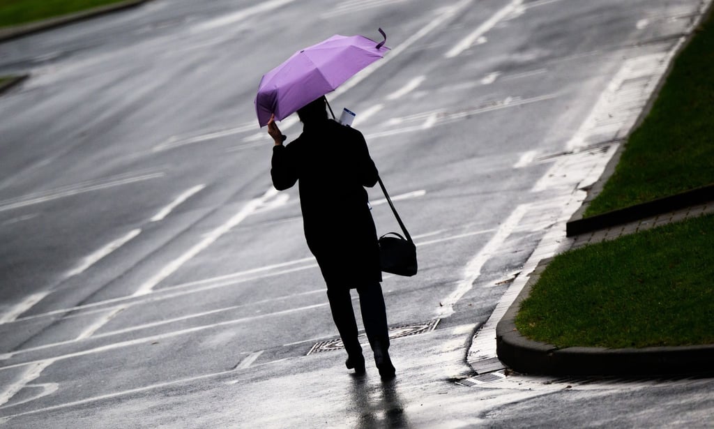 Eine Frau geht bei stürmischem Regenwetter mit Regenschirm über das Messegelände Hannover.