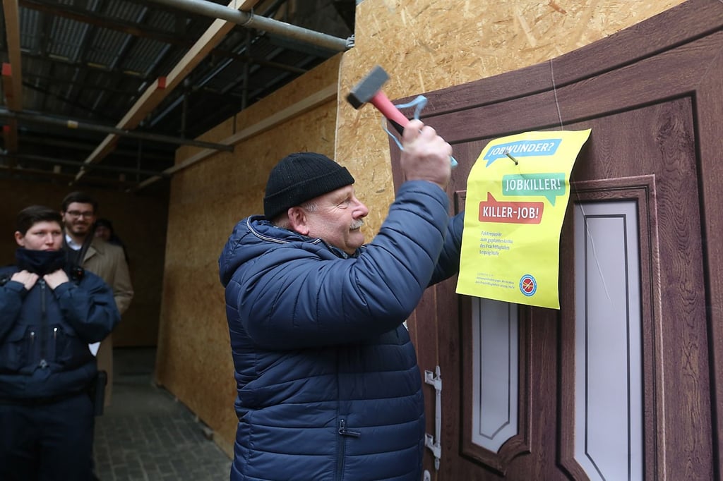 Peter Richter von der IG Nachtflugverbot nagelt nach dem Vorbild von Luthers Thesenanschlag in Wittenberg symbolisch ein Forderungspapier an eine Papptür an der Ulrichskirche. 