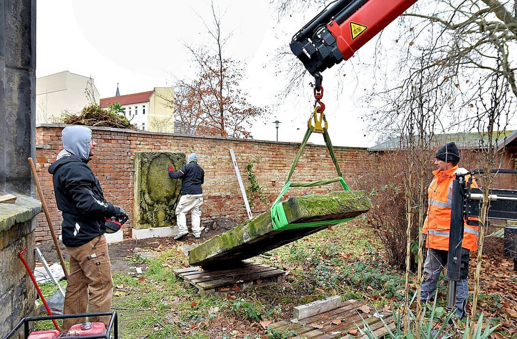 Mit einem Kran wird die Gedenktafel zur Mauer gehoben. Diese war vorab von ihrem Efeu-Bewuchs befreit worden.