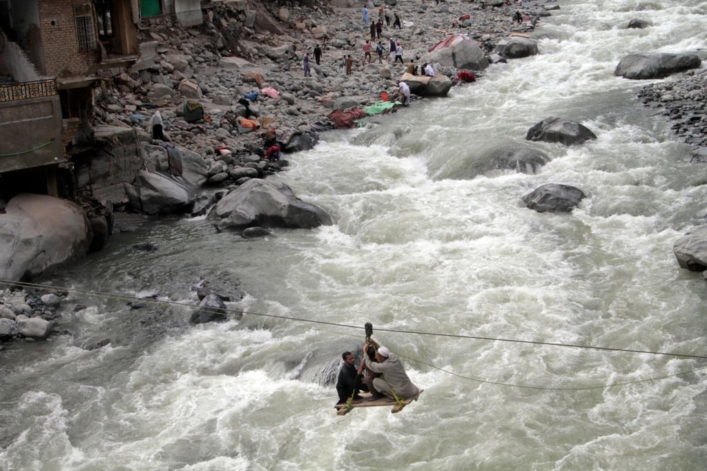 Nach schweren Überschwemmungen überqueren Menschen im pakistanischen Bahrain einen Fluss mithilfe einer Seilbahn.