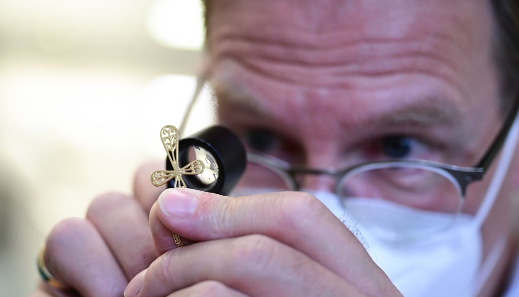 Ein Mitarbeiter einer Pfandleihe taxiert ein Kreuz einer Goldkette mit einer Lupe.