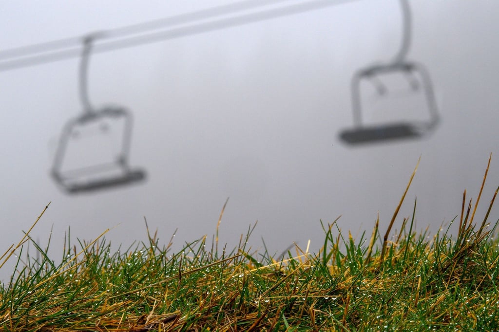Wassertropfen hängen im Gras vom Skihang "Hexenritt". Im Hintergrund ist der Sessellift im Nebel zu sehen.