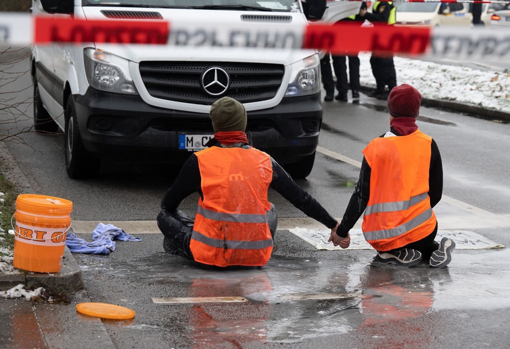 Bei Nieselregen und Minusgraden blockieren Klimaaktivisten der Gruppe Letzte Generation eine Straße in München.