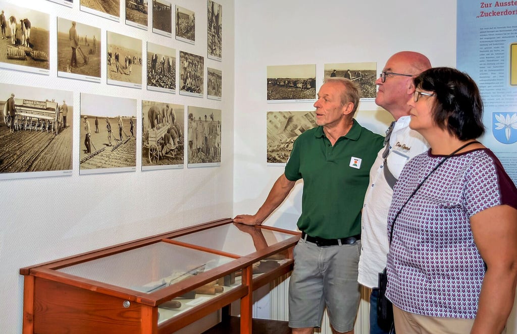 Olaf Wachsmuth (links) vom Kulturverein in Klein Wanzleben erläutert Besuchern die historischen Fotografien zum Zuckerrübenanbau in der Region.