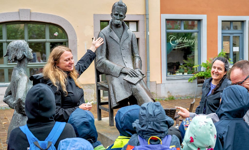 Bibliotheksmitarbeiterin Antje Key und Catarina Caetano da Rosa, stellvertretende Leiterin des Nietzsche-Dokumentationszentrums, mit Kindern des Hortes der Lebenshilfe am Nietzsche-Denkmal auf dem Naumburger Holzmarkt.