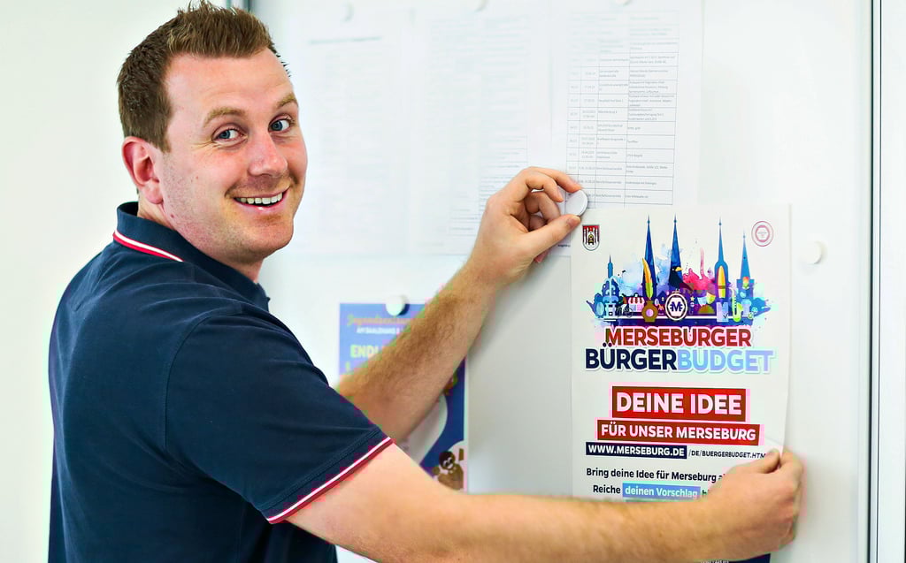 Florian Schüler, der Leiter des Jugend- und Sportamtes, bringt im Rathaus eine Plakat an, das fürs Bürgerbudget werben soll.