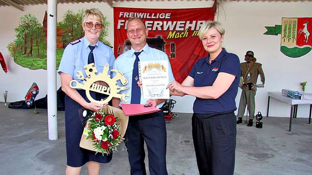 Ortswehrleiterin Gudrun Ganske (links) und die Bürgermeisterin Cathleen Lüdicke ehren Matthias Hupka für 30 Jahre aktive Mitarbeit in der Wehr und überreichen die Urkunde „Oldtimer-Doktor“.