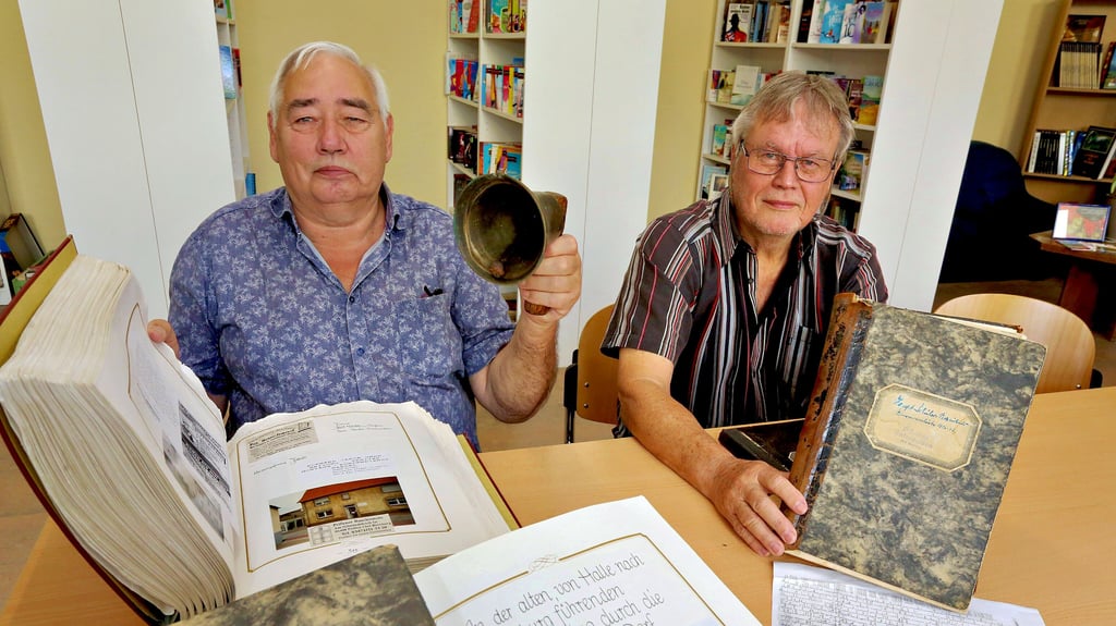 Hans-Jürgen Berg (links) und Karl-Heinz Groth stöbern in Peißens Archiven. Mit der Glocke ging früher der Gemeindediener durch das Dorf und berichtete der Bevölkerung von den neuesten Begebenheiten aus dem Rathaus.