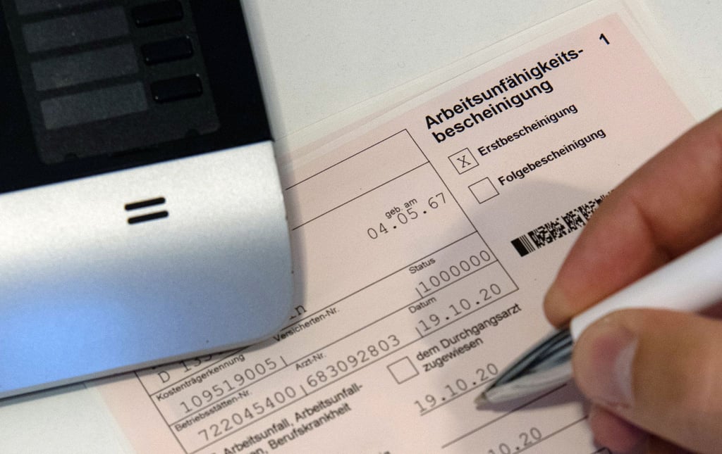 Ein Mitarbeiter einer Arztpraxis notiert etwas auf einer Arbeitsunfähigkeitsbescheinigung.