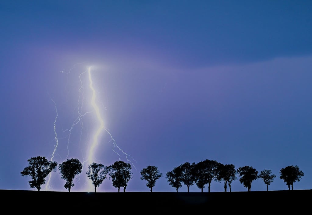 Ein Blitz eines Gewitters erhellt den Nachthimmel über der Landschaft im Osten des Landes Brandenburg.