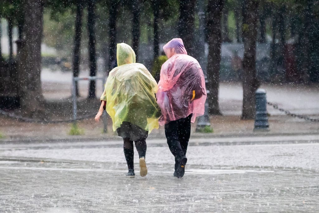 Menschen mit Plastik-Regenschutz gehen durch den Regen.