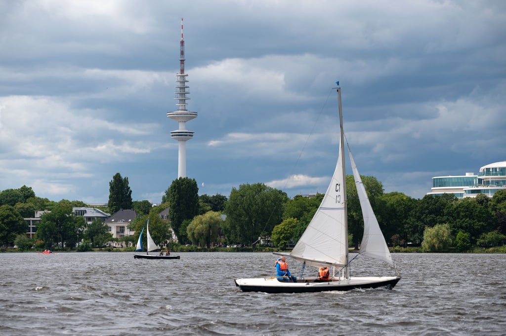 Dunkle Wolken ziehen über den Fernsehturm und die Außenalster, auf der Segelboote kreuzen.