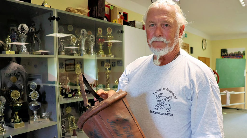 Karl-Heinz Pick zeigt ein historisches Löschgerät. Ledereimer waren für jedes Haus Pflicht. Auf dem Eimer ist „W. Pütsch Schönhausen“ als Beschriftung zu erkennen.