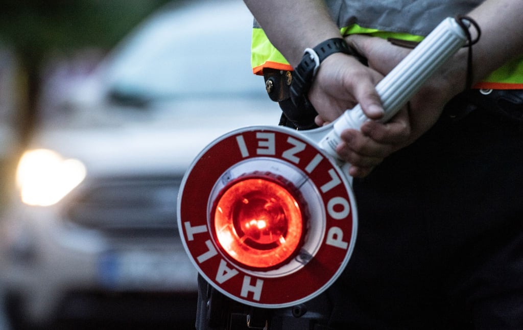 Ein Polizist hält bei einer Verkehrskontrolle eine Winkerkelle in der Hand.