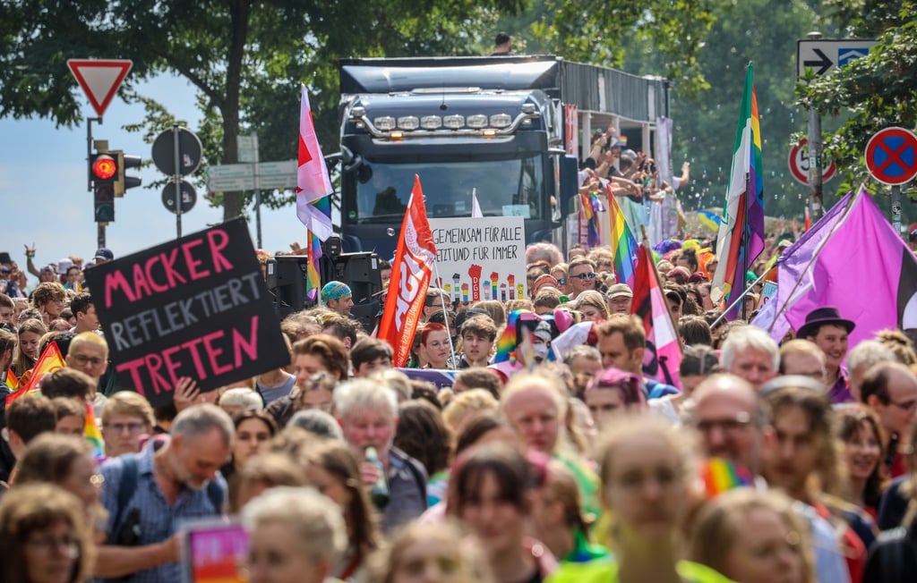Teilnehmer des CSD gehen in Bremen mit einem Fahnen und Schildern den Sielwall entlang.
