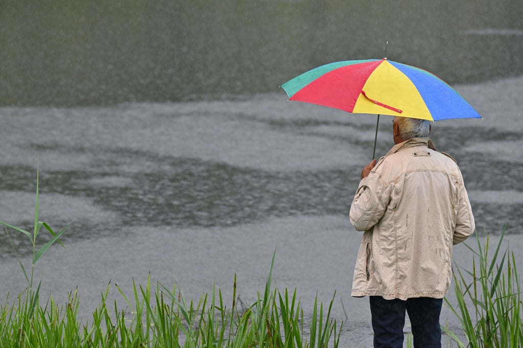 Ein Mann mir Regenschirm steht am Fluss Schwarze Elster.