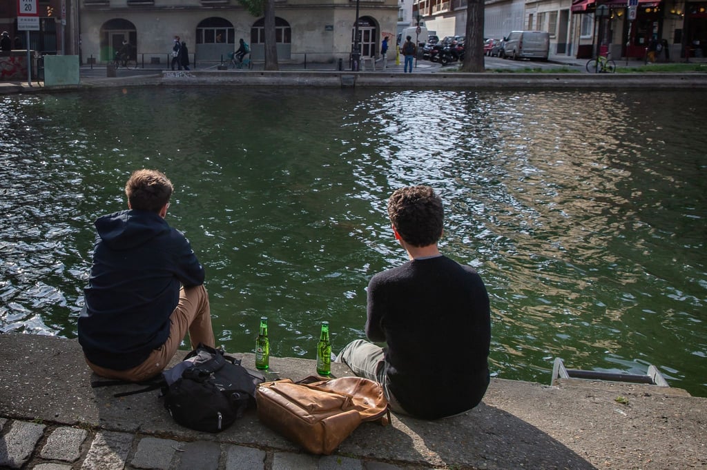 Zwei junge Männer trinken am Ufer des Kanals Saint-Martin in Paris gemeinsam Bier.