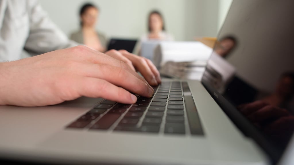 Ein Mann tippt einem Büro auf einer Tastatur eines Laptops.