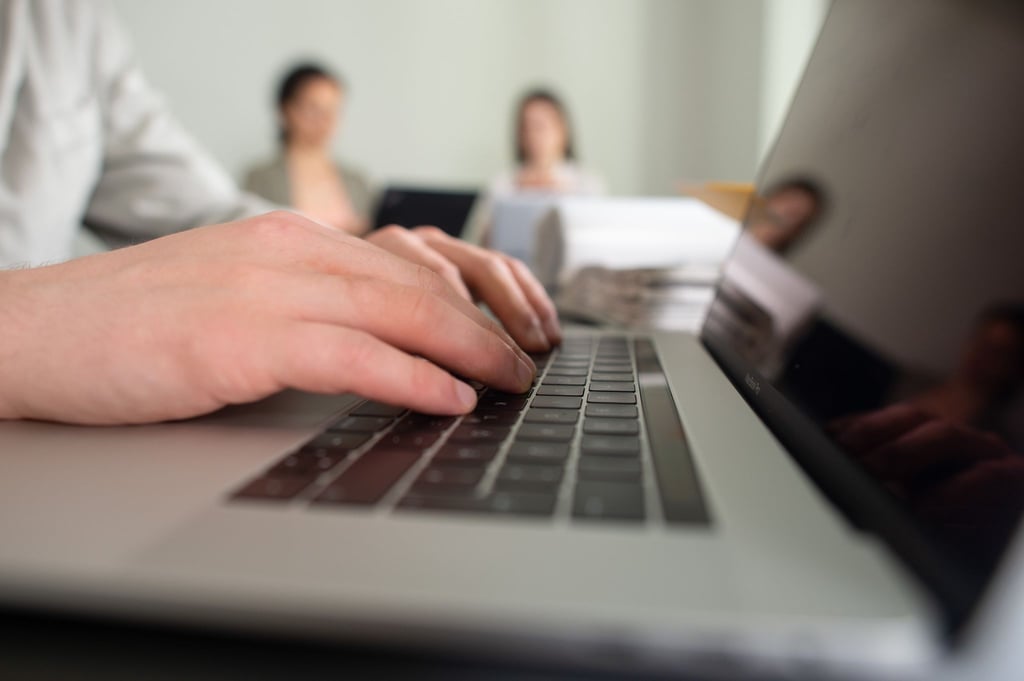 Ein Mann tippt einem Büro auf einer Tastatur eines Laptops.