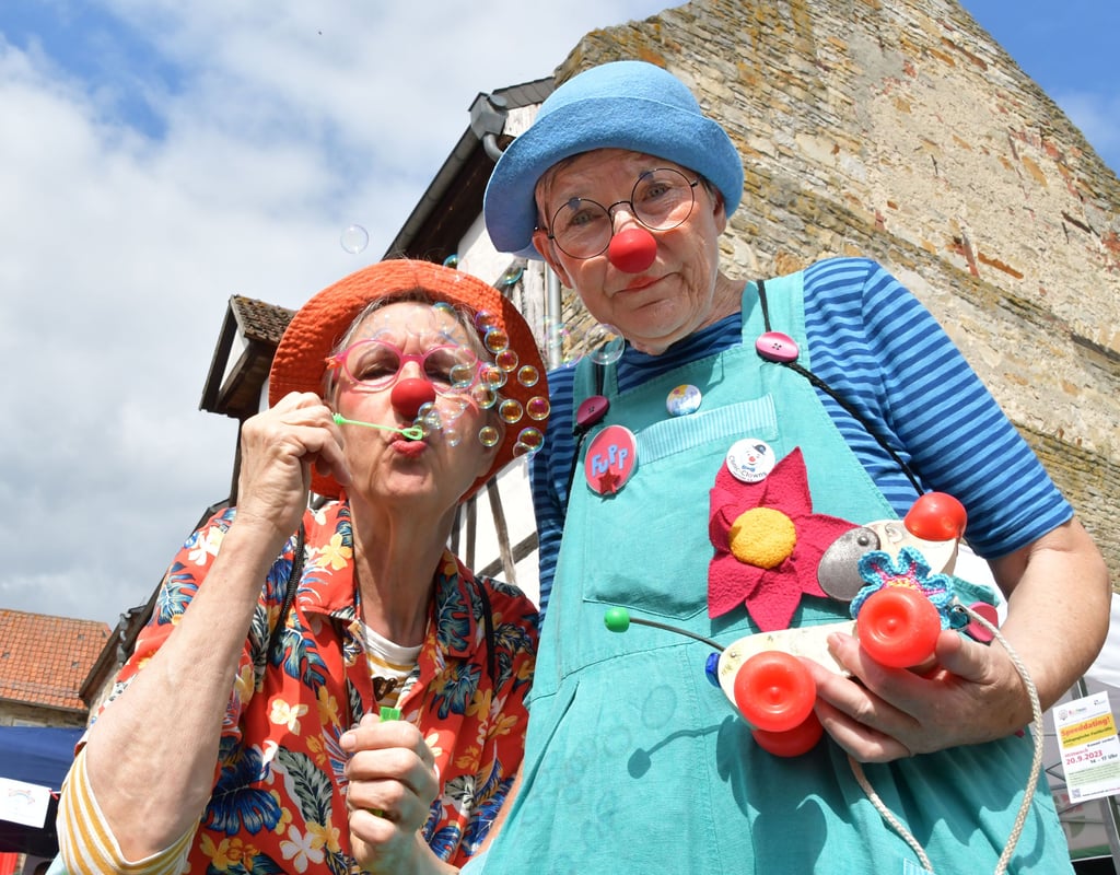 Zwei Clown-Damen mit einem Hund auf Rädern sorgen für Unterhaltung.